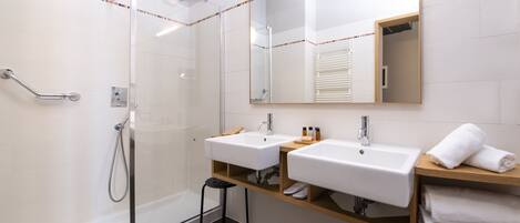 Un baño moderno con dos lavabos, un espejo grande y una ducha con mampara de vidrio.