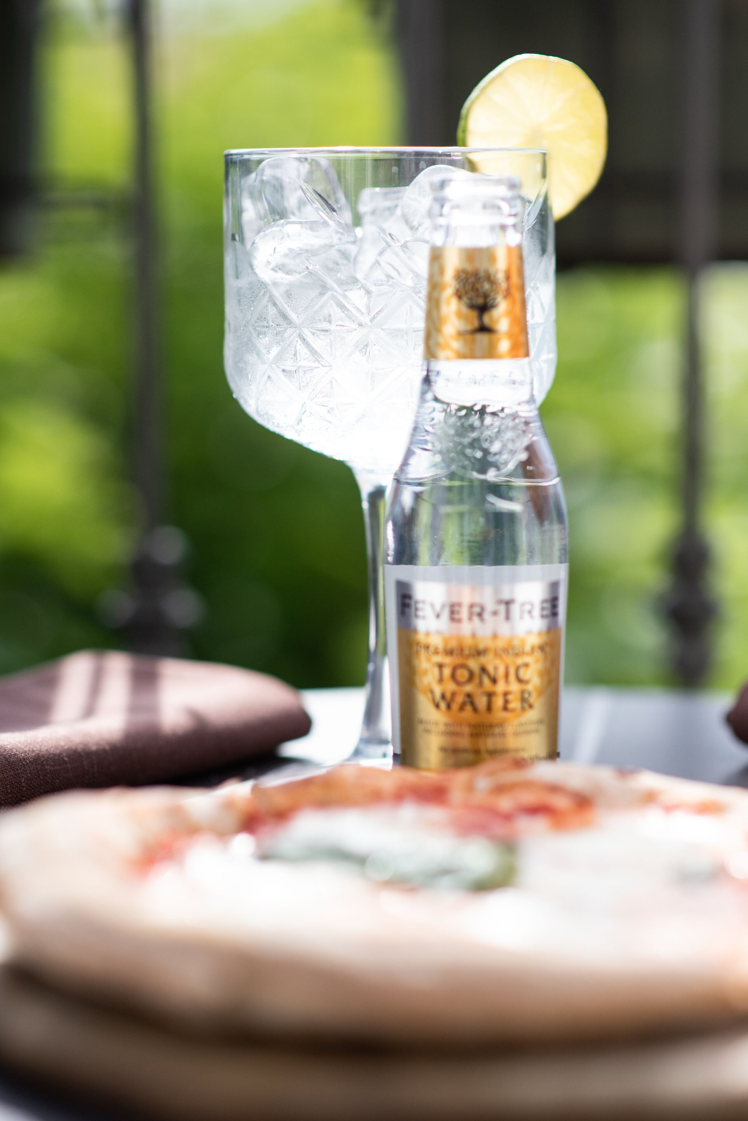 Een glas tonic met een citroenpartje op een tafel, met een fles waarop staat 