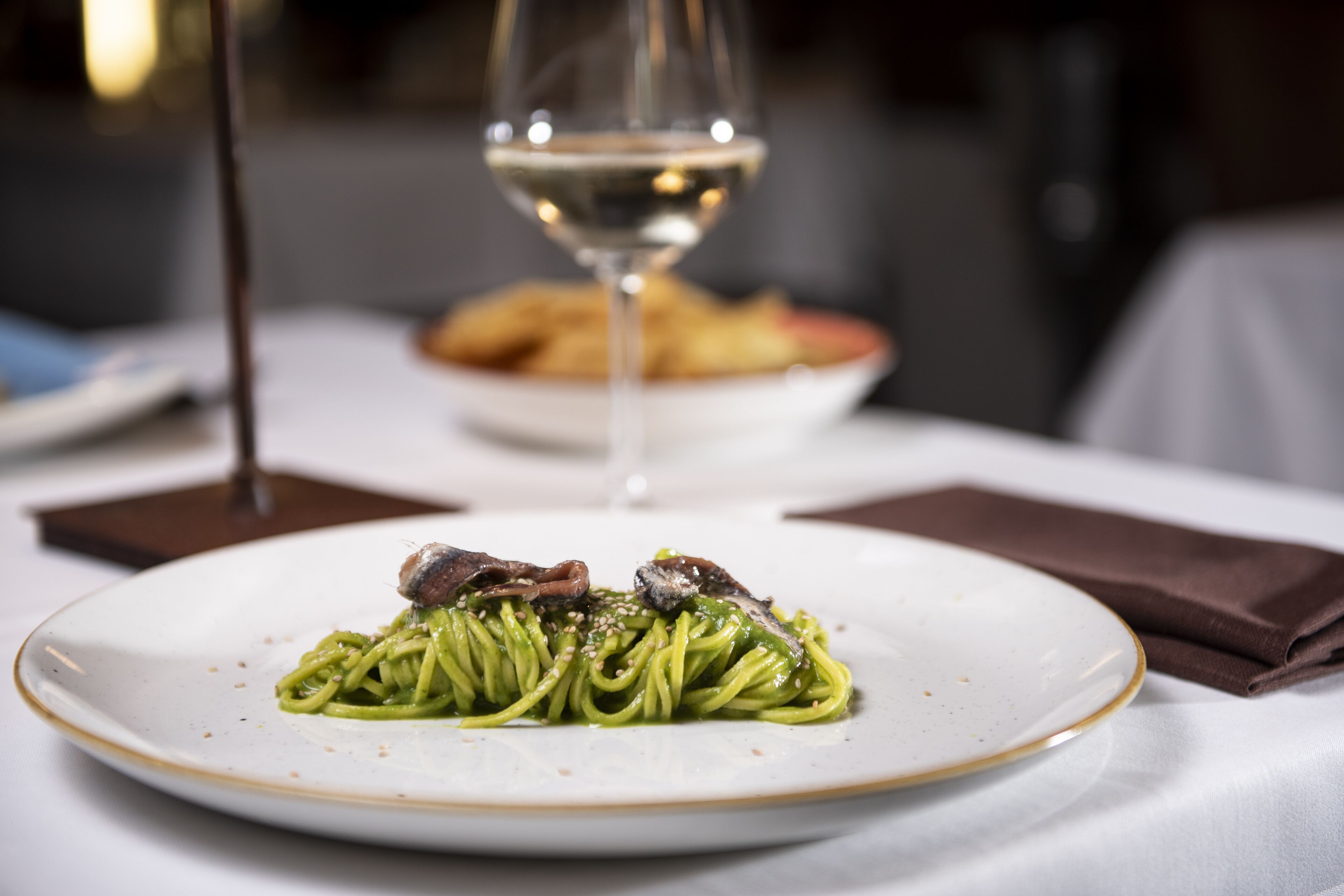 A plate of pasta with a glass of white wine on a table.