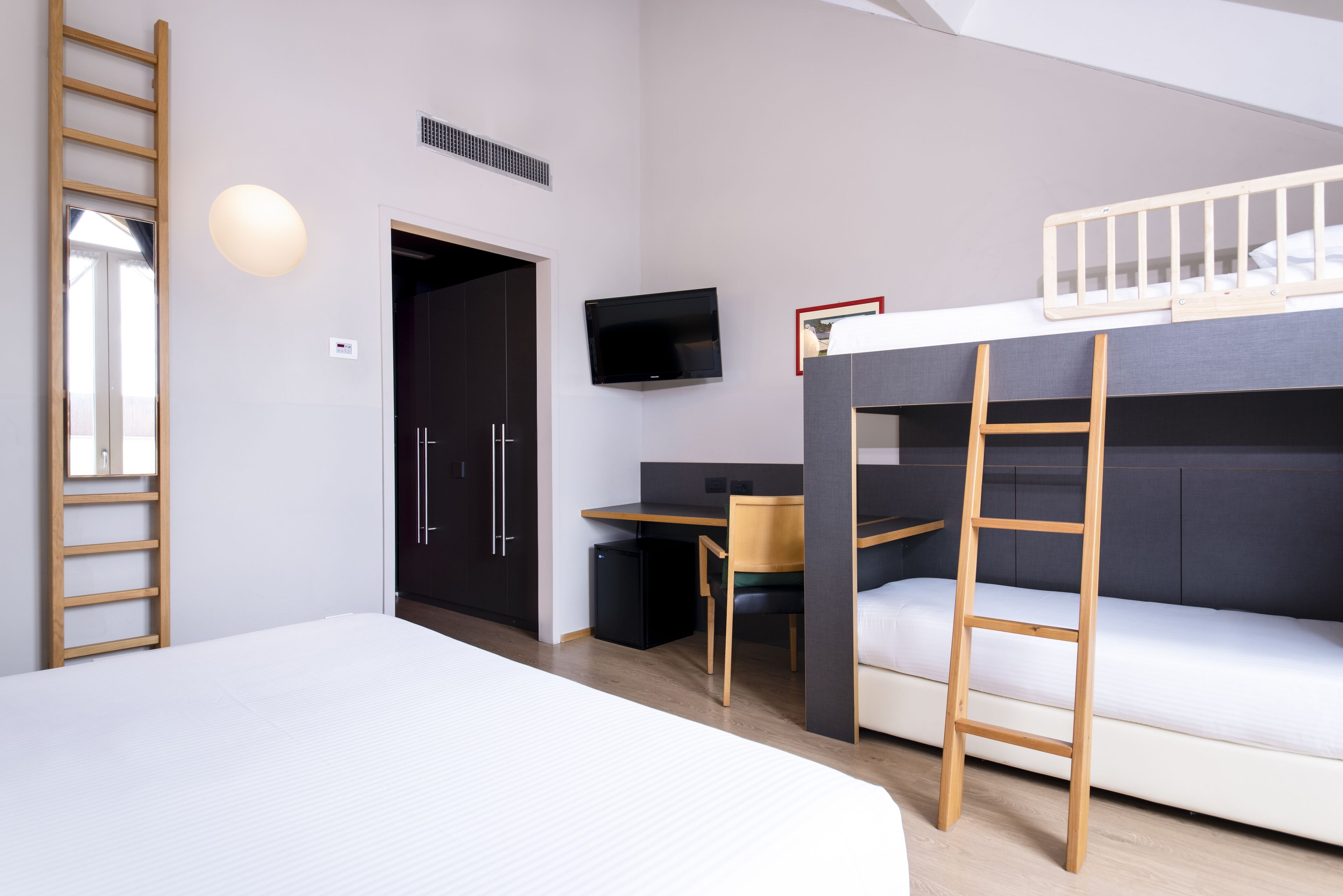 A modern room with a bunk bed, a desk, a chair, a TV, and a ladder.