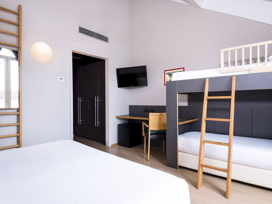 A modern room with a bunk bed, a desk, a chair, a TV, and a ladder.