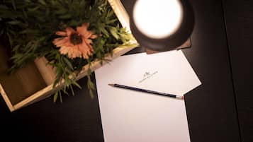 Une caisse en bois contenant une fleur, une feuille de papier blanche ornée d’un logo et un crayon posés sur une surface sombre.