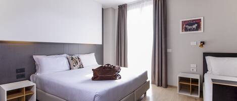 A modern hotel room with a large bed, a nightstand, a small table, and a window with curtains.