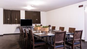 Un salón de conferencias con una mesa grande, sillas, un televisor y cortinas.