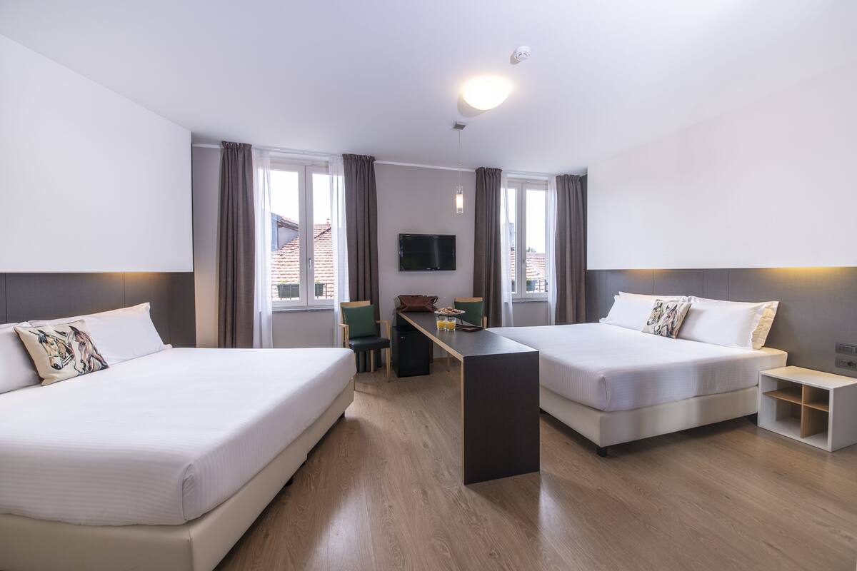 Een hotelkamer met twee bedden, een bureau, een stoel, een televisie en grote ramen.