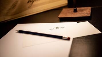 Un foglio di carta con un logo e del testo, una matita e una piccola scatola di legno su una superficie scura.