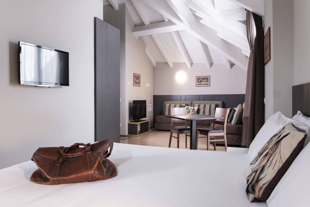 Een hotelkamer met een bed, een bureau, een stoel, een televisie en een leren tas.