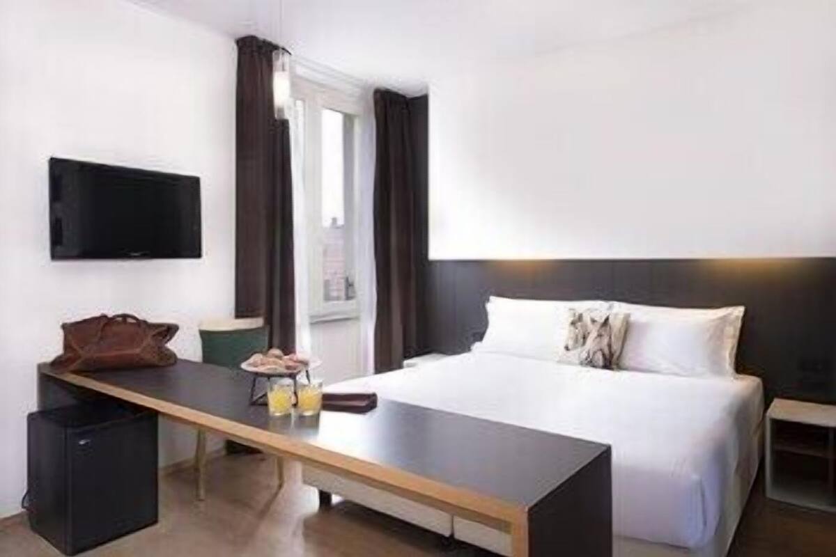 Een hotelkamer met een bed, een bureau, een televisie en een raam met gordijnen.
