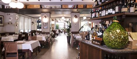 A restaurant interior with tables, chairs, a bar area with wine bottles, and a large decorative bottle of wine corks.