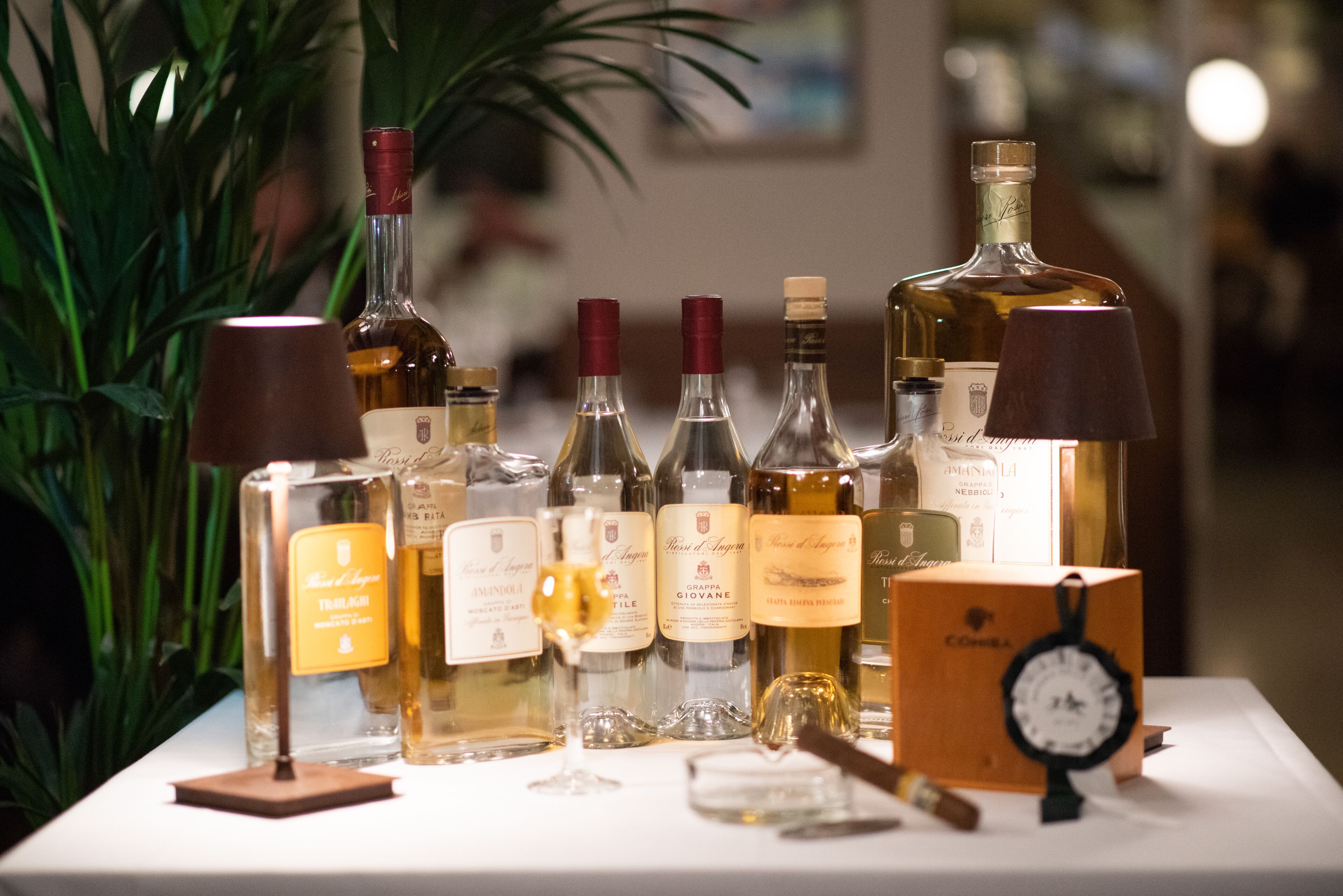 Una exhibición de diversas botellas de alcohol, incluyendo vino y licores, dispuestas sobre una mesa con un reloj y una lámpara.