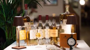 Una exhibición de diversas botellas de alcohol, incluyendo vino y licores, dispuestas sobre una mesa con un reloj y una lámpara.
