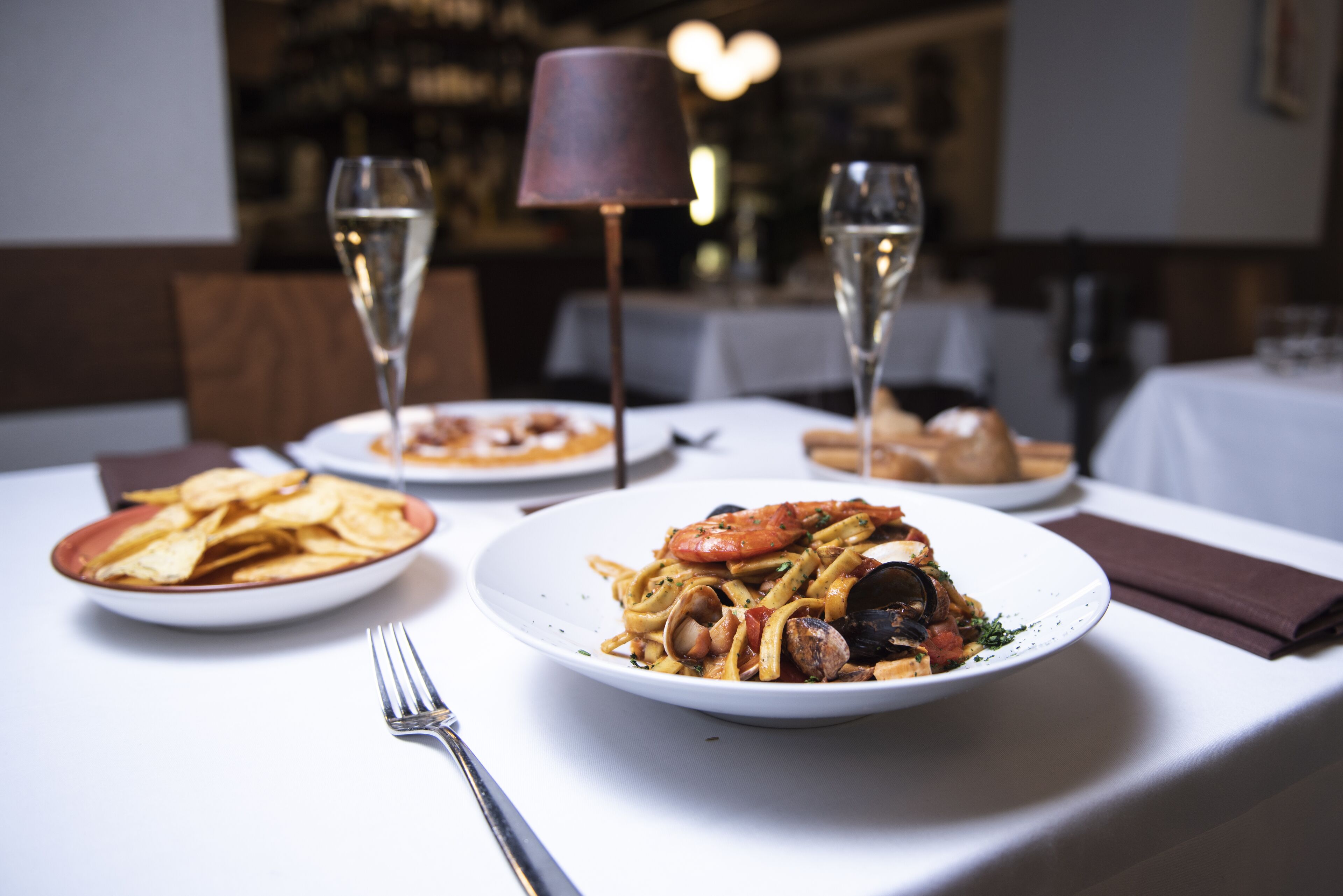 Ein Esstisch mit Pasta, Chips, einer Gabel und zwei Weingläsern.