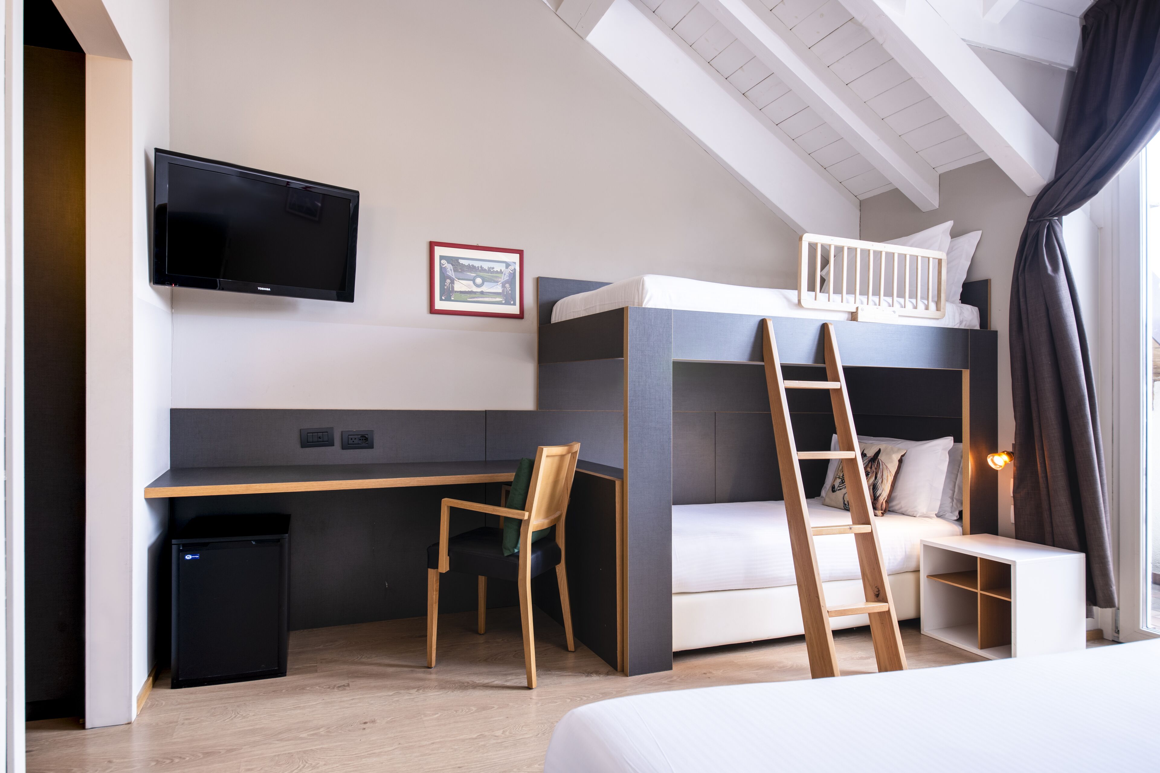 A modern bedroom with a bunk bed, a desk, a chair, a TV, and a small trash bin.