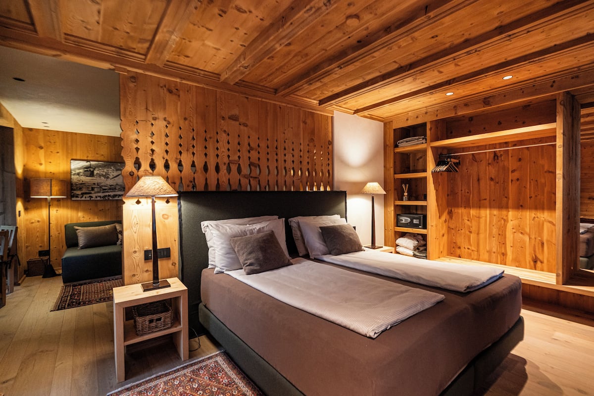 A wooden-paneled bedroom with a large bed, two bedside tables, and a wardrobe.