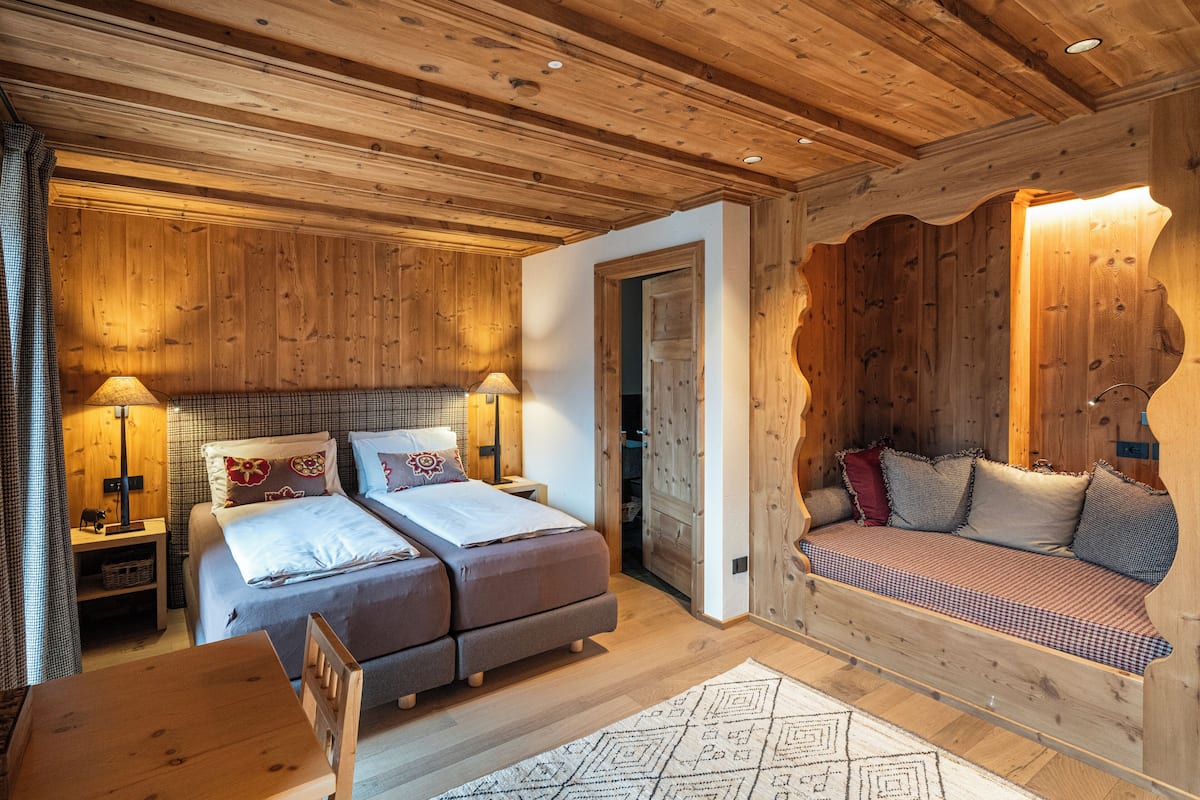 A cozy wooden cabin room with two beds, a sofa, and a dining table.