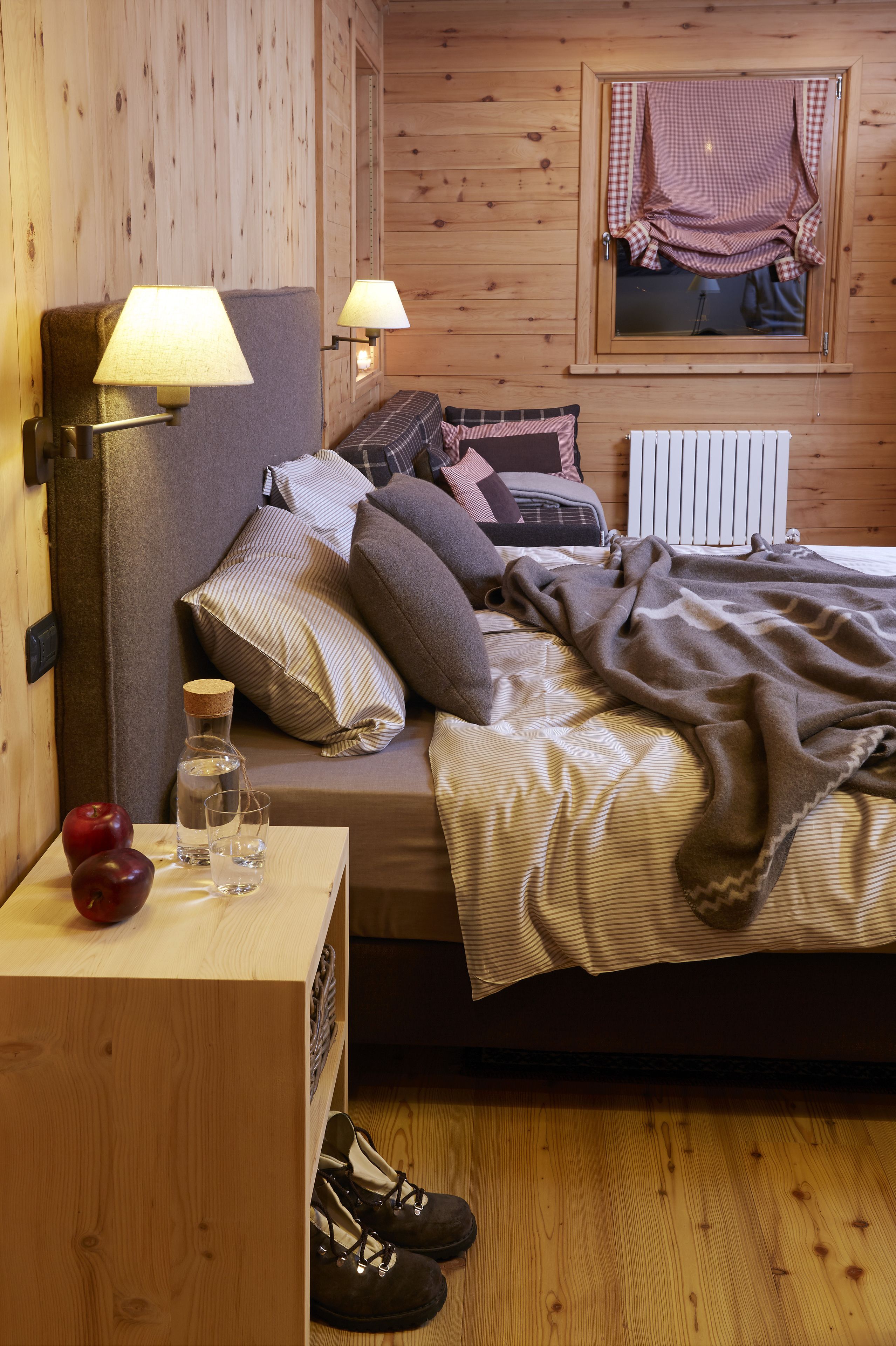 A cozy room with a bed, pillows, a blanket, a nightstand with a lamp, a bottle, and a glass.