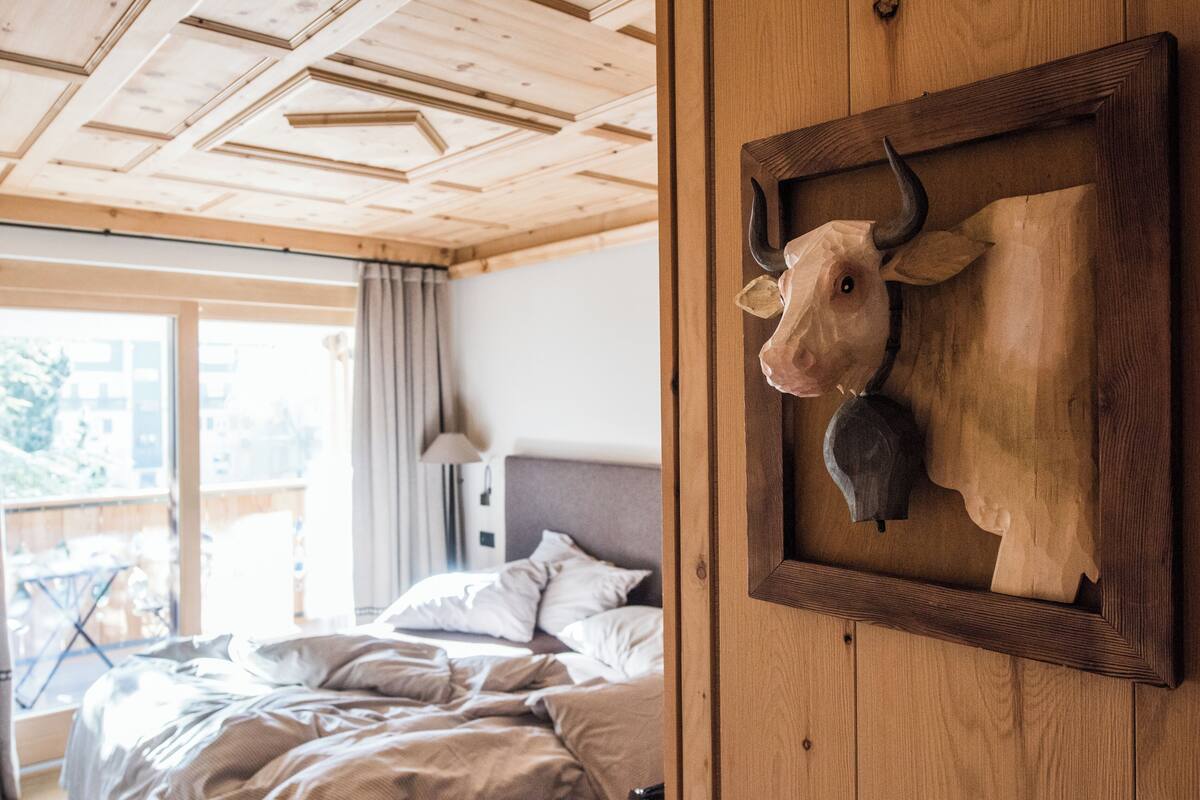 A bedroom with a bed, wooden ceiling, and a cow head decoration on the wall.