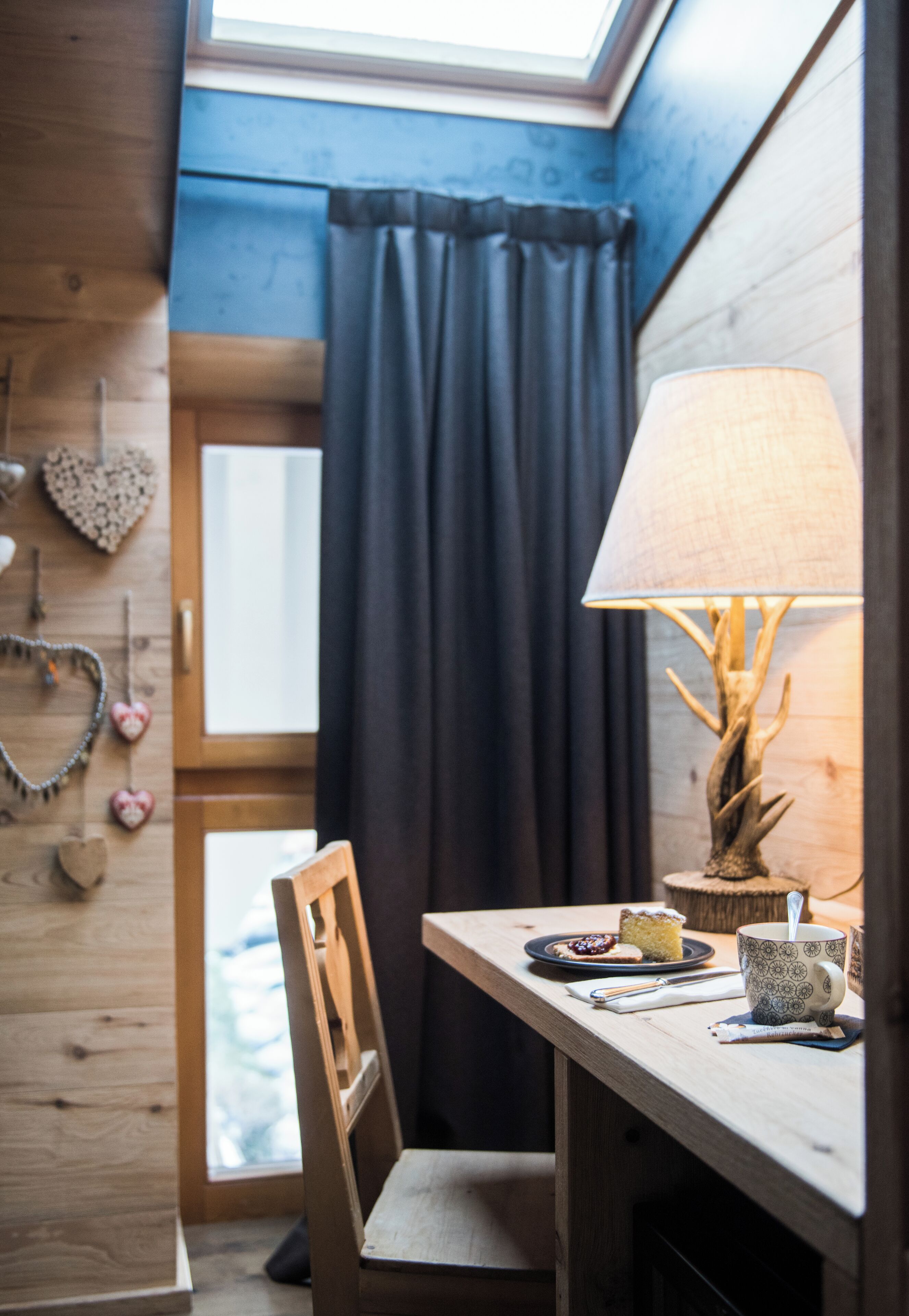 A cozy room with a wooden table, a lamp, and a view of the outdoors through a window with curtains.