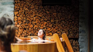 A wooden hot tub with a stone wall backdrop.