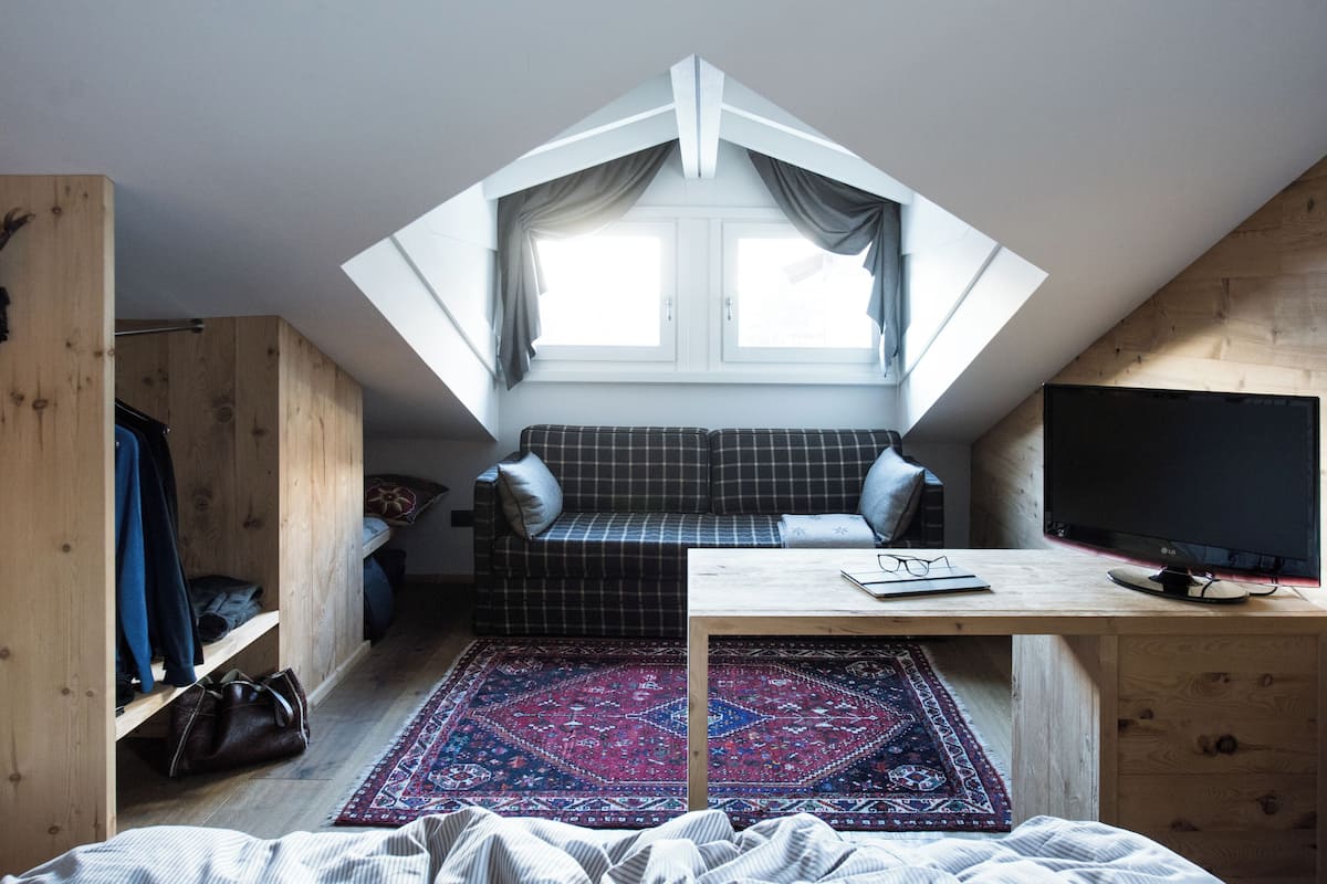 A cozy attic bedroom with a sloped ceiling, a plaid sofa, a television, and a wooden wardrobe.