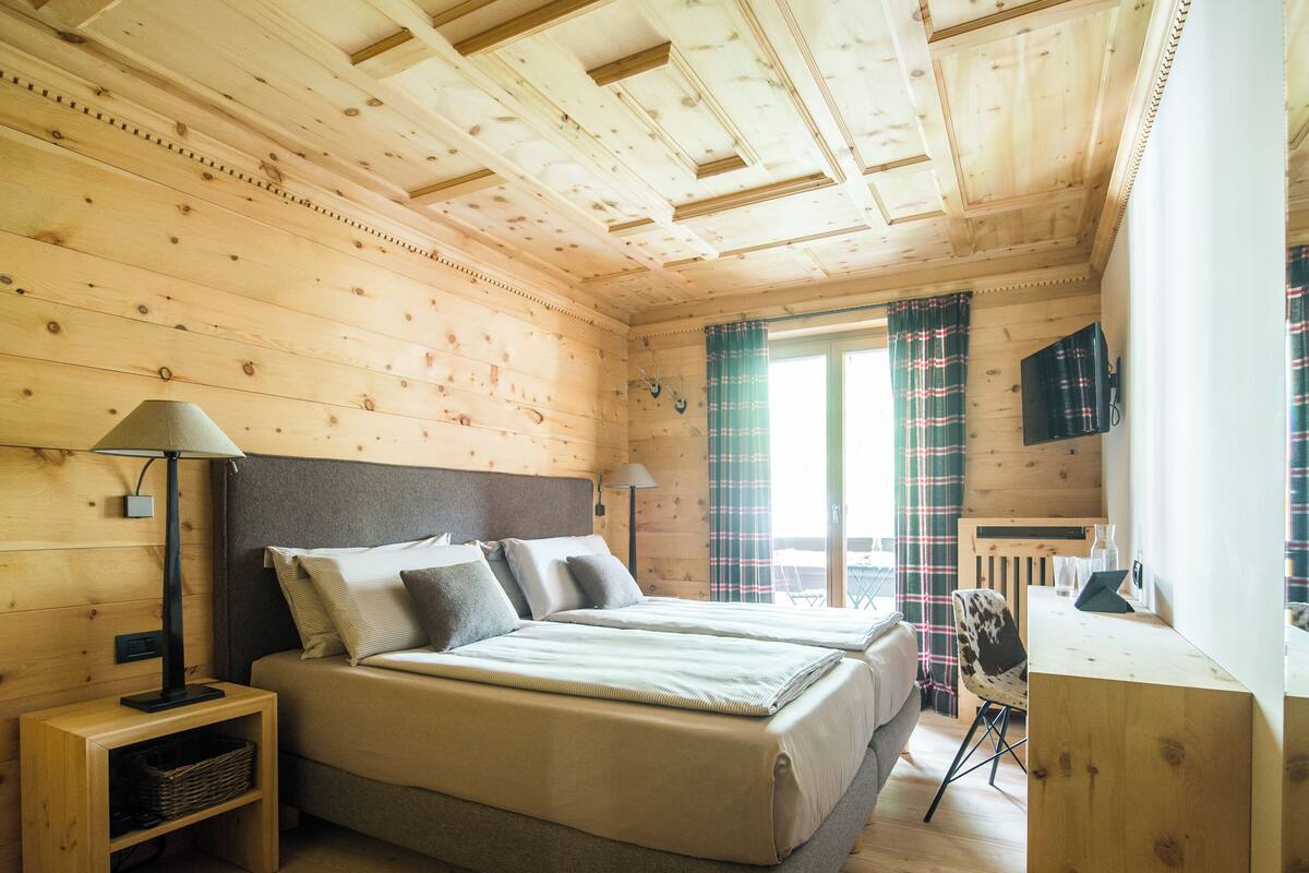 A wooden cabin bedroom with two beds, a desk, and a chair.