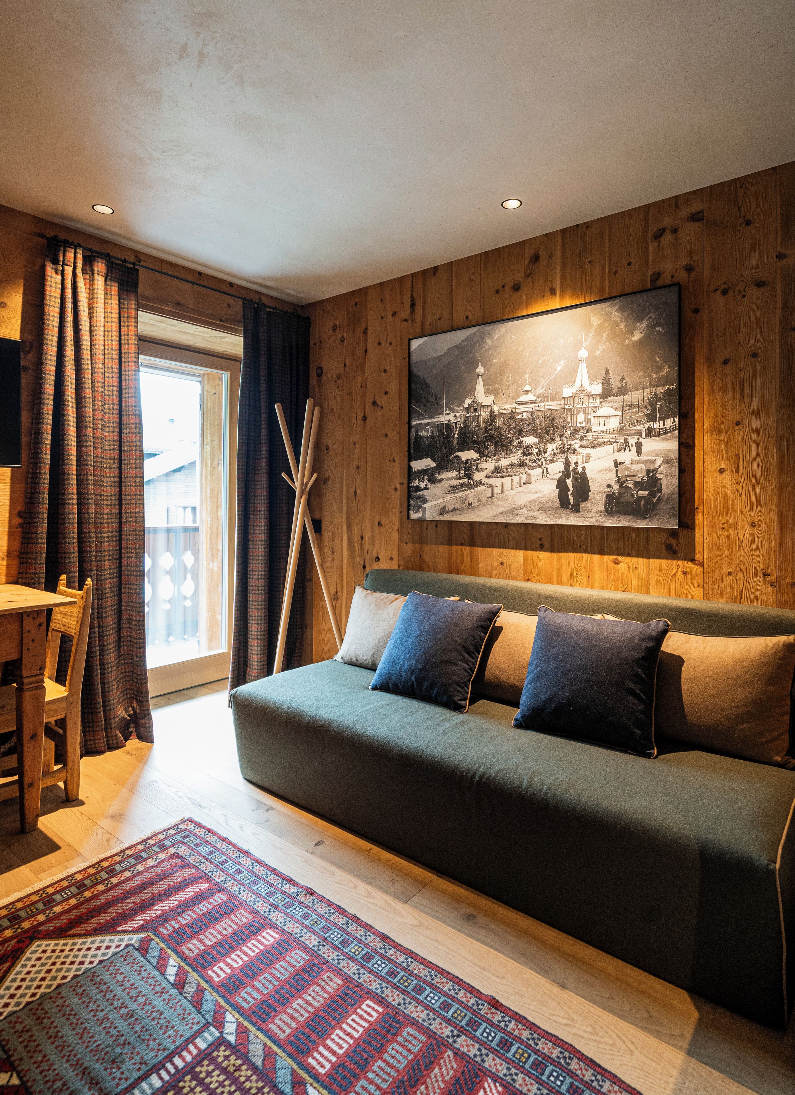 Un salon chaleureux avec un mur en bois, une grande photo encadrée, un canapé avec des coussins, un tapis à motifs et un coin repas avec une table et des chaises.