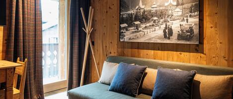 Un salon chaleureux avec un mur en bois, une grande photo encadrée, un canapé avec des coussins, un tapis à motifs et un coin repas avec une table et des chaises.