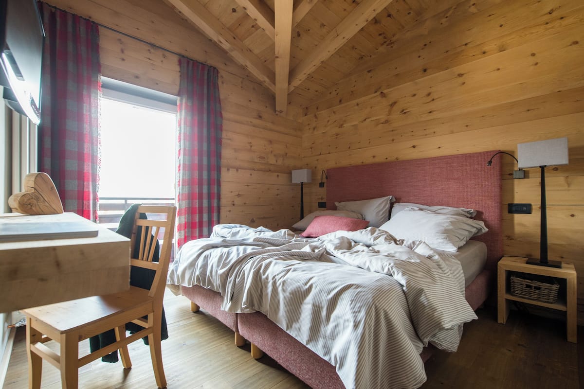 A wooden cabin bedroom with a bed, bedside tables, a desk, and a chair.