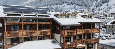 A multi-story building with balconies, a snow-covered landscape, and mountains in the background.