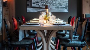 A dining table set with glasses and plates, surrounded by chairs, in a room with wooden walls and a framed picture on the wall.