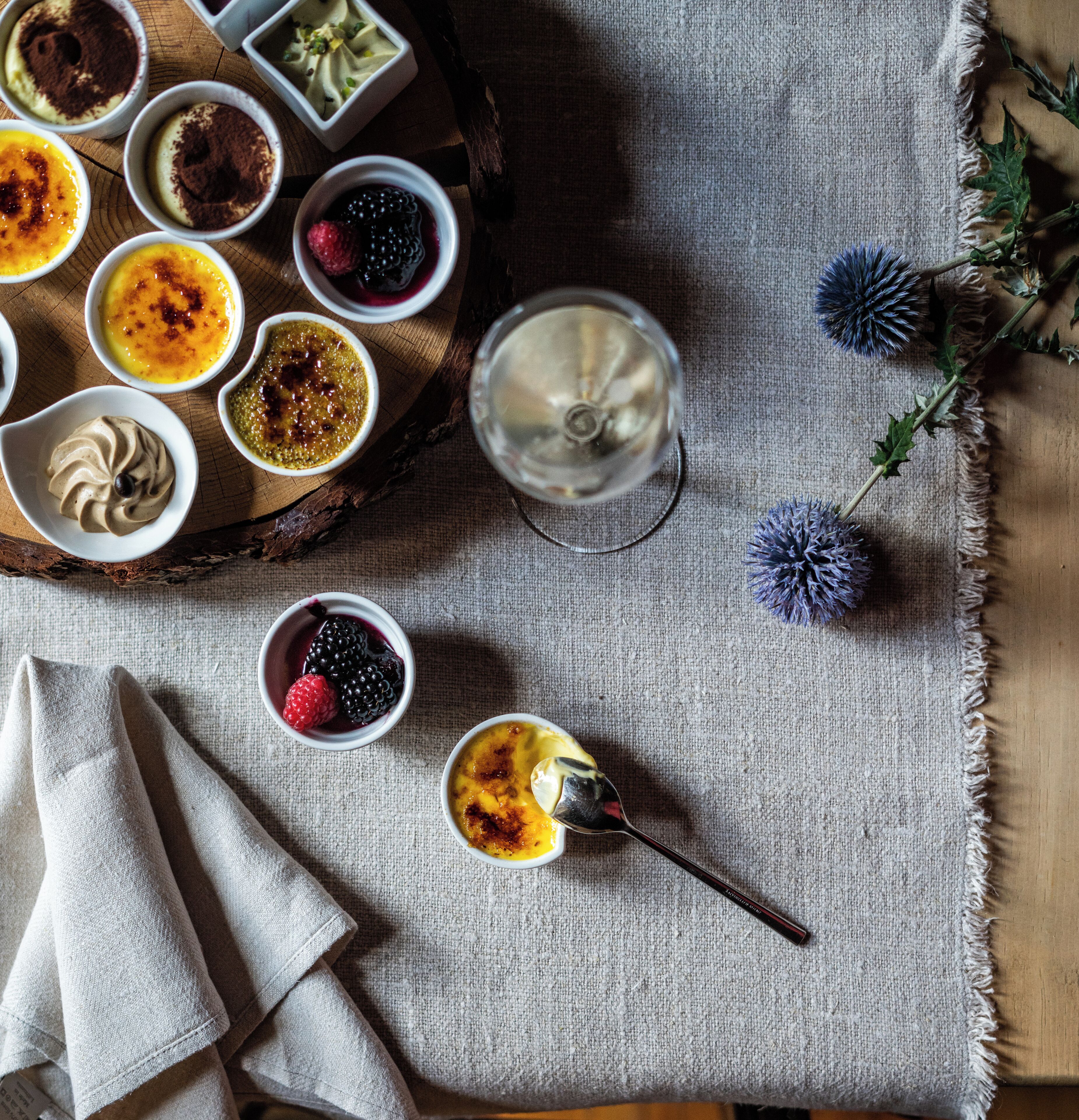 A variety of desserts on a wooden tray, a glass of white beverage, and a napkin on a textured fabric surface.