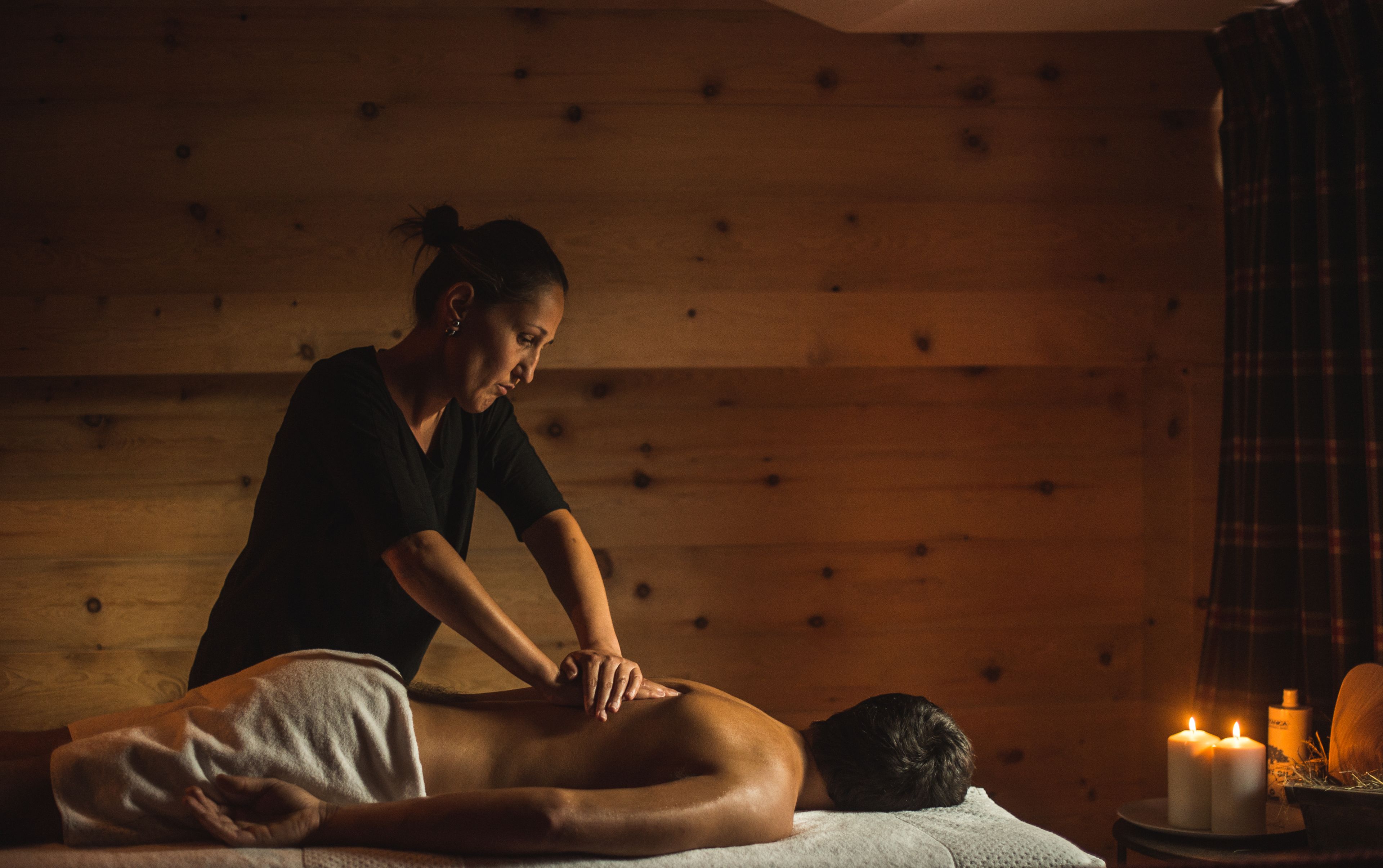 Une séance de massage dans une pièce aux murs en bois, dans une ambiance tamisée à la lumière des bougies.