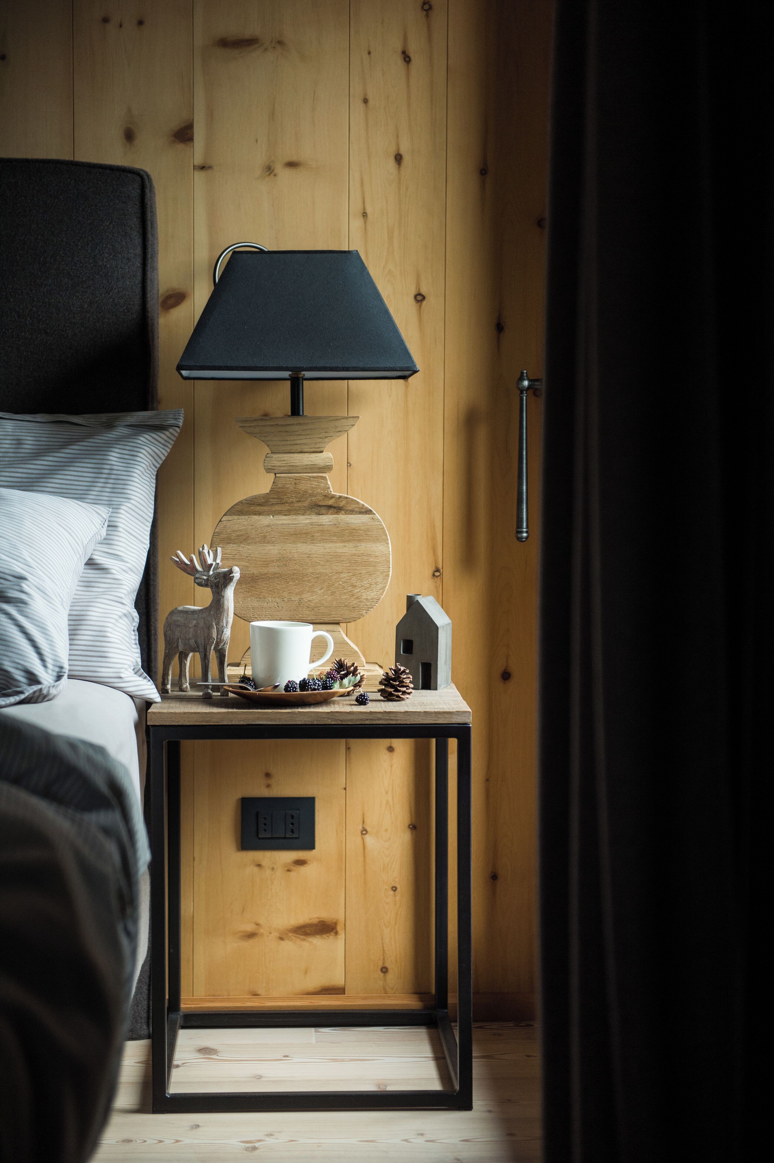 Una mesita de noche de madera con una lámpara, una taza, un modelo de casa y una figurita de reno.