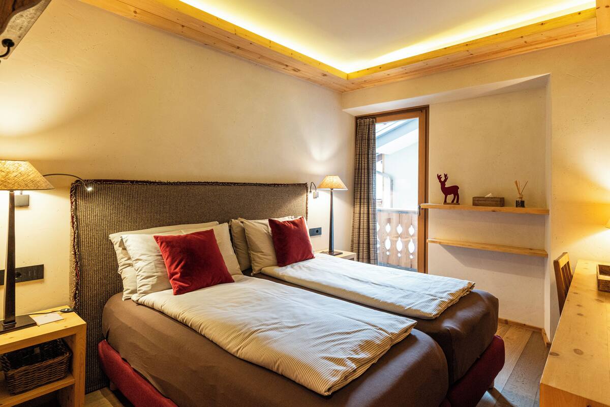 A double bed with a headboard, bedside lamps, a small table with a lamp, and a shelf with a decorative item.