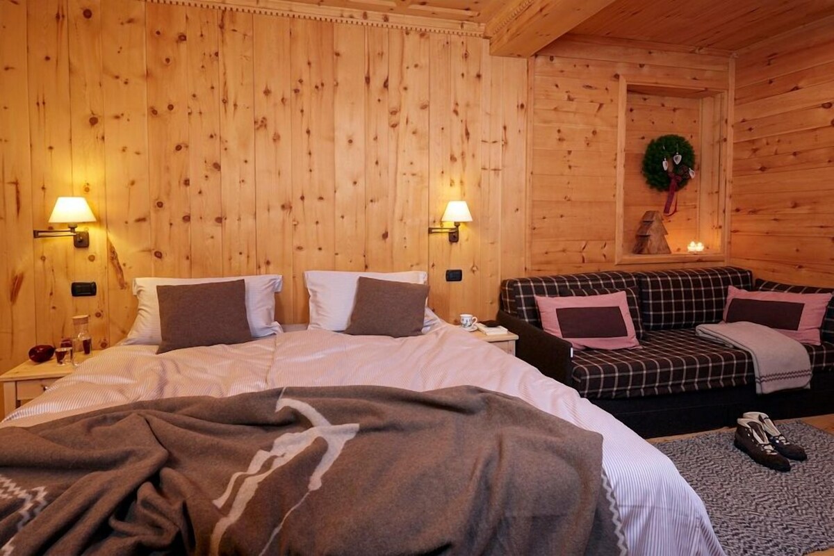 Um quarto aconchegante de madeira com uma cama, um sofá e duas luminárias na parede.