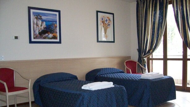 A room with two beds, a chair, and two framed pictures on the wall. - Hotel Tre Leoni (Somma Lombardo)