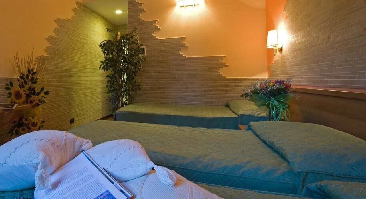 A room with a bed, a wall-mounted light, and a plant.