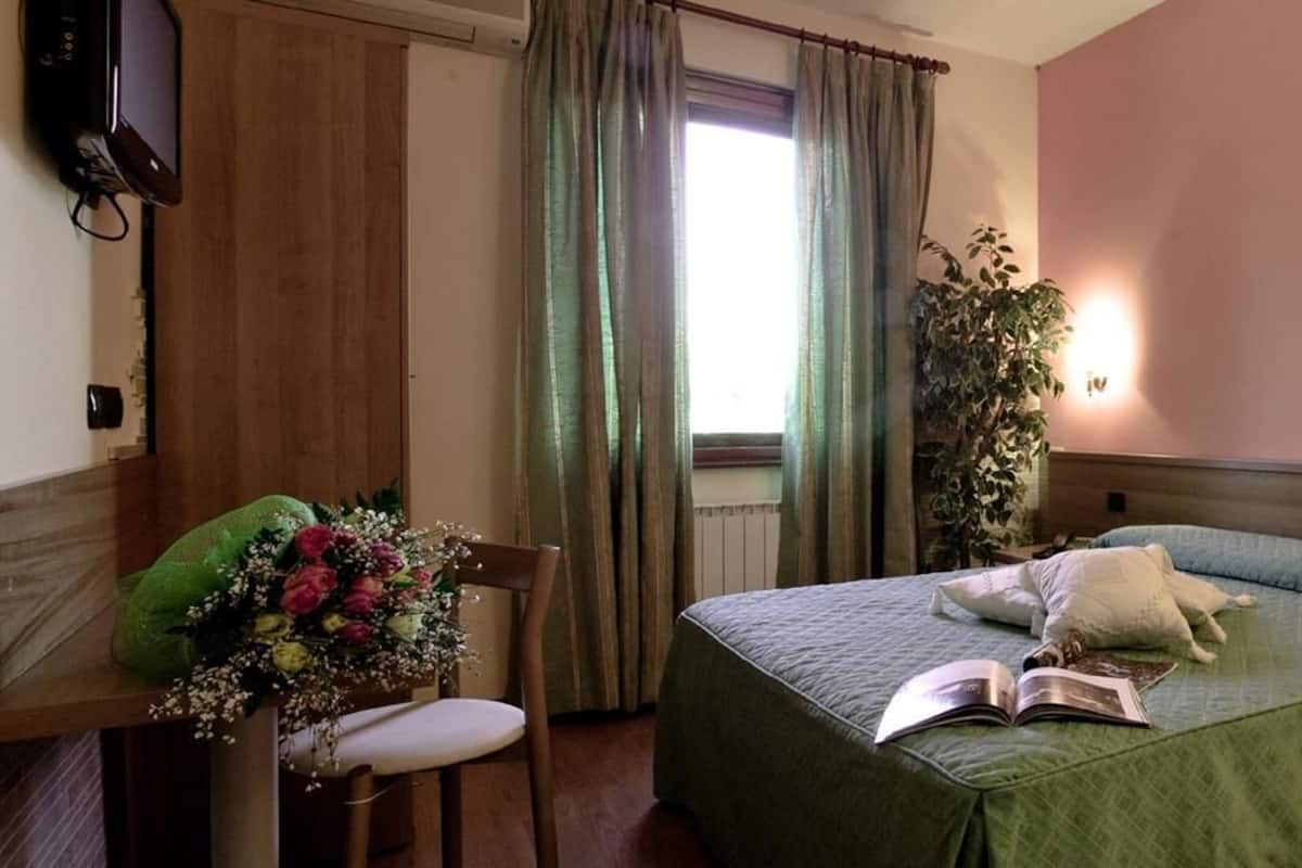 A hotel room with a bed, a desk with a chair, a television, and a window with curtains.
