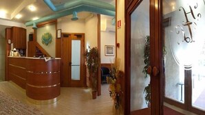 A reception area with a wooden reception desk, a staircase, and potted plants. - Hotel Tre Leoni (Somma Lombardo)
