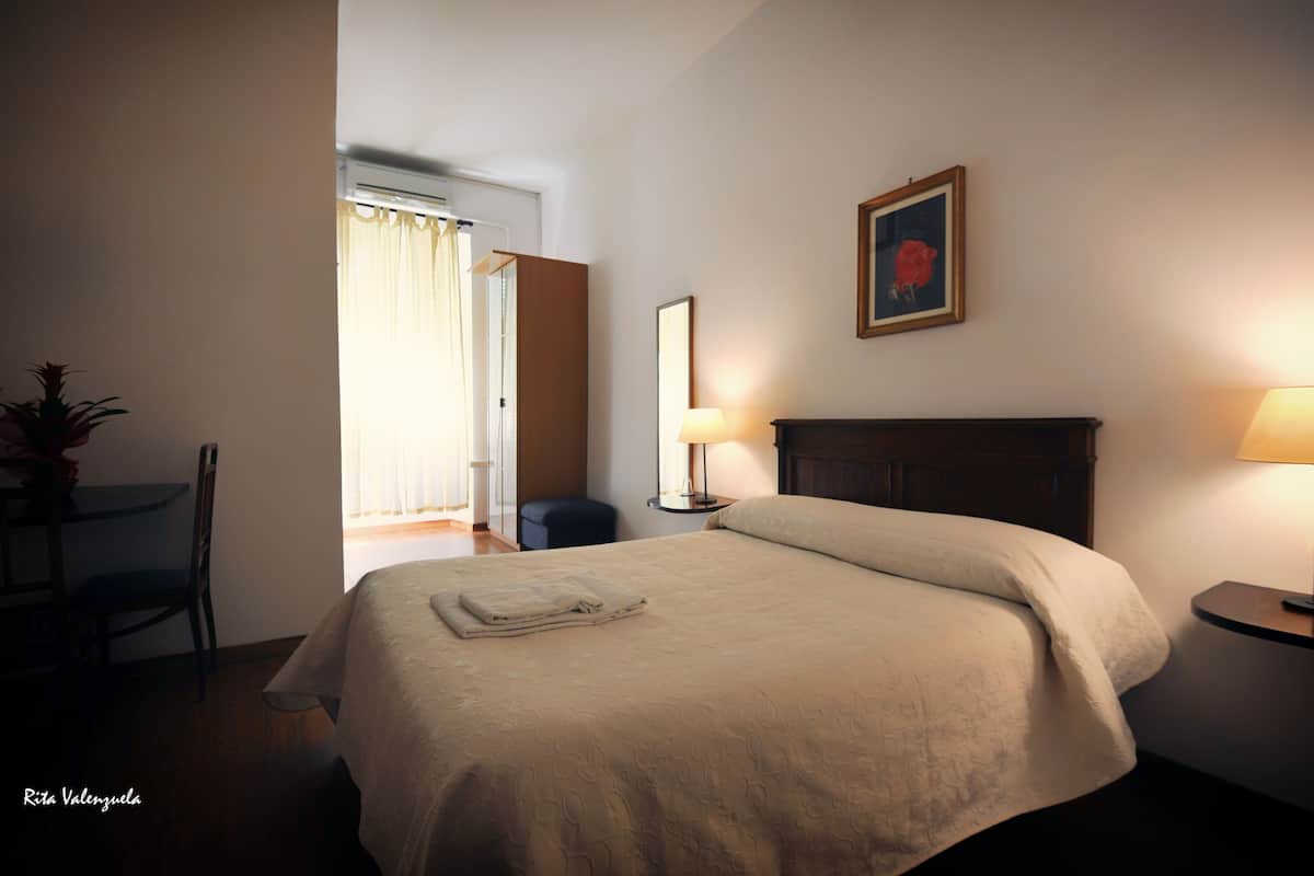 A hotel room with a bed, a chair, a table with a lamp, and a painting on the wall.