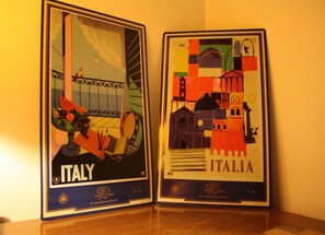 Dos obras de arte enmarcadas que representan Italia, una con vista a una ventana y la otra con detalles arquitectónicos.