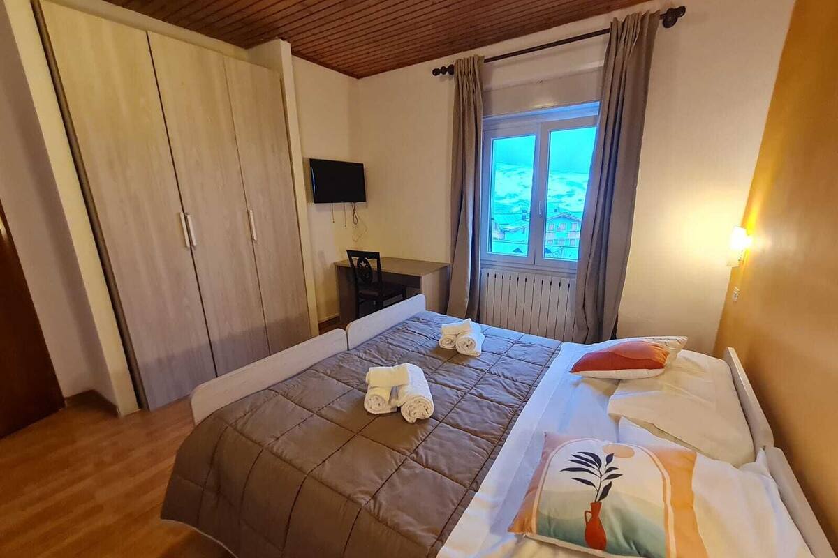 Een slaapkamer met een bed, een bureau, een televisie en een raam met gordijnen.