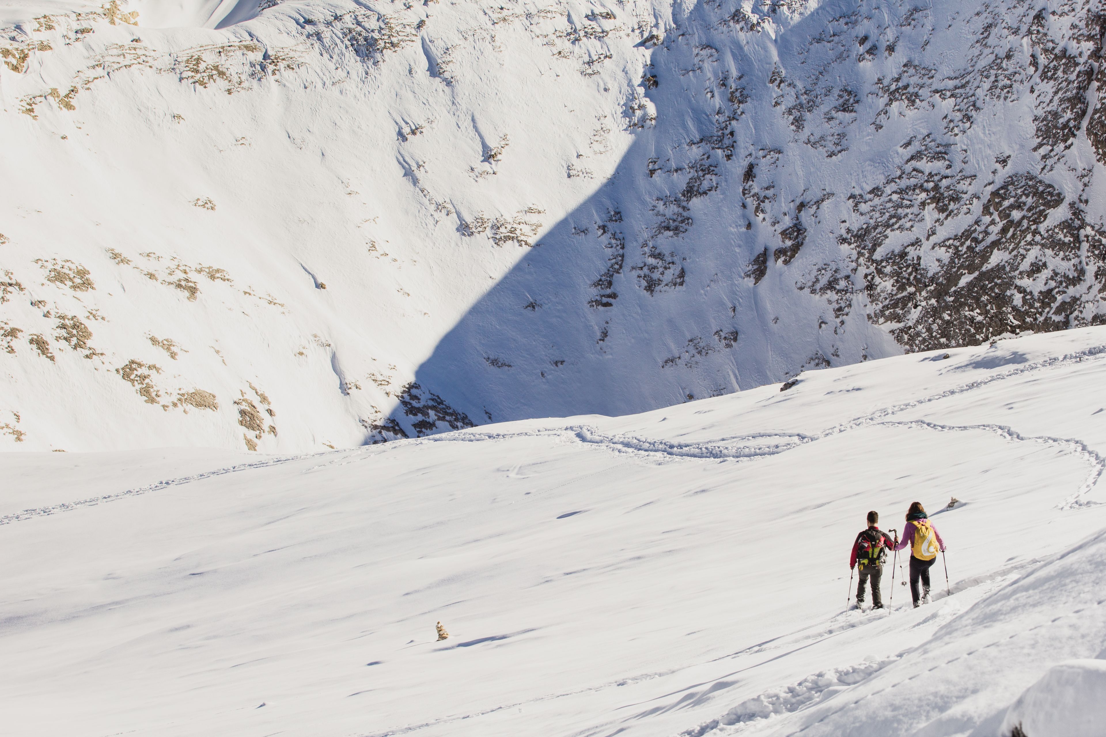 A snowy mountain landscape with two skiers descending a slope.