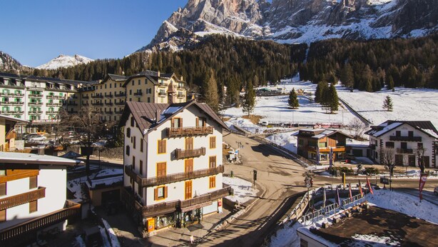A mountain town with snow-covered streets and buildings, including a hotel with balconies and a view of the mountains.