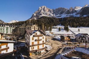 Un paese di montagna con strade e palazzi imbiancati dalla neve, tra cui un albergo con balconi e vista sulle montagne.