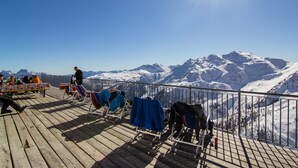 A wooden deck with chairs and tables, overlooking a snow-covered mountain range.