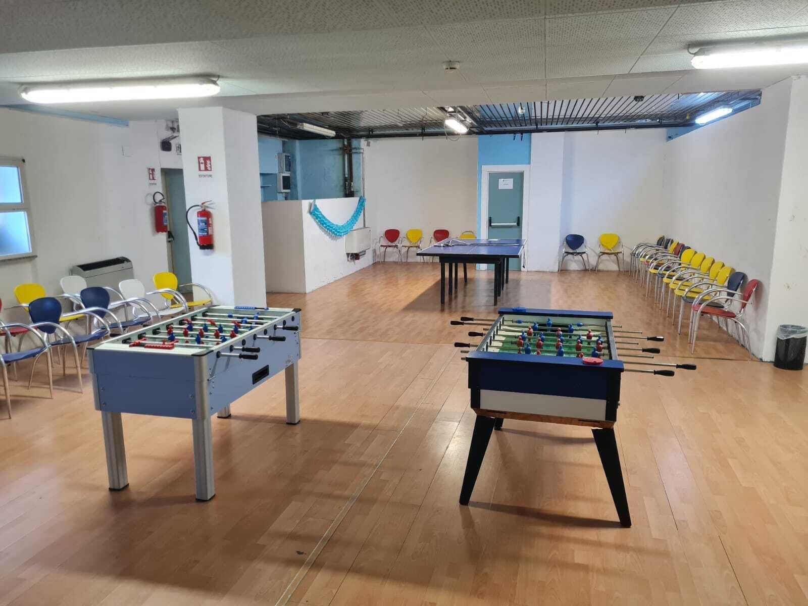 A room with two foosball tables, chairs, a fire extinguisher, and a blue curtain.