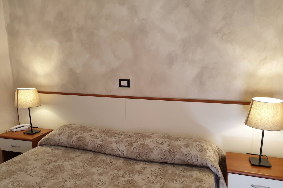 A hotel room with a bed, two bedside tables, a lamp on each table, and a phone on one of the tables.