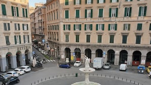 Une place circulaire avec une fontaine centrale, entourée de bâtiments historiques aux volets verts.