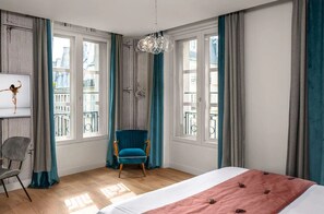 Un dormitorio con una cama grande, una silla, un televisor y vistas a edificios a través de amplios ventanales.